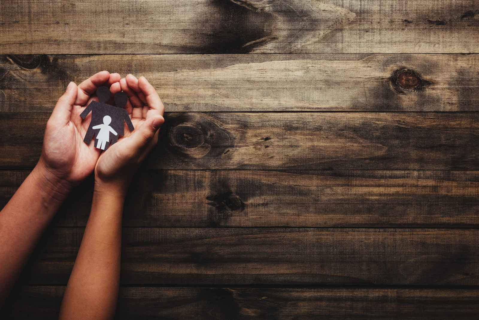 Manos que sostienen una figura de papel de un adulto con un niño, sobre una mesa de madera
