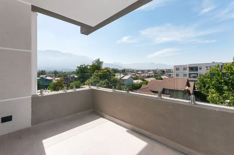 Terraza de un departamento con baranda de vidrio y vista a casas bajas y a la cordillera.